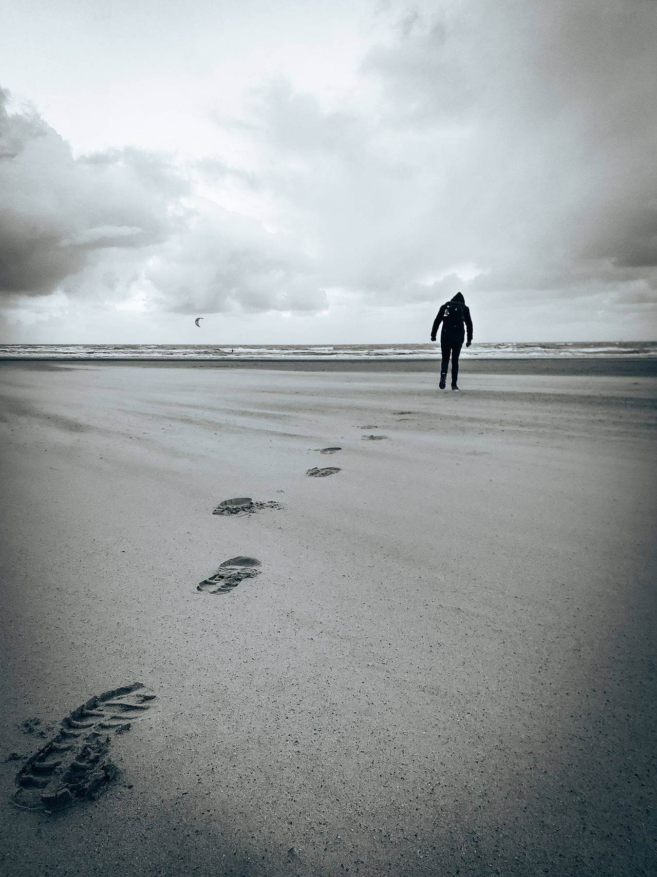 Person geht über einen windigen Strand, Fußspuren im Sand