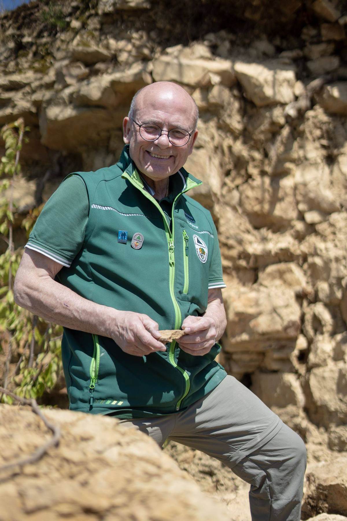 Matthias kniet vor der Gesteinswand und zeigt ein Fossil