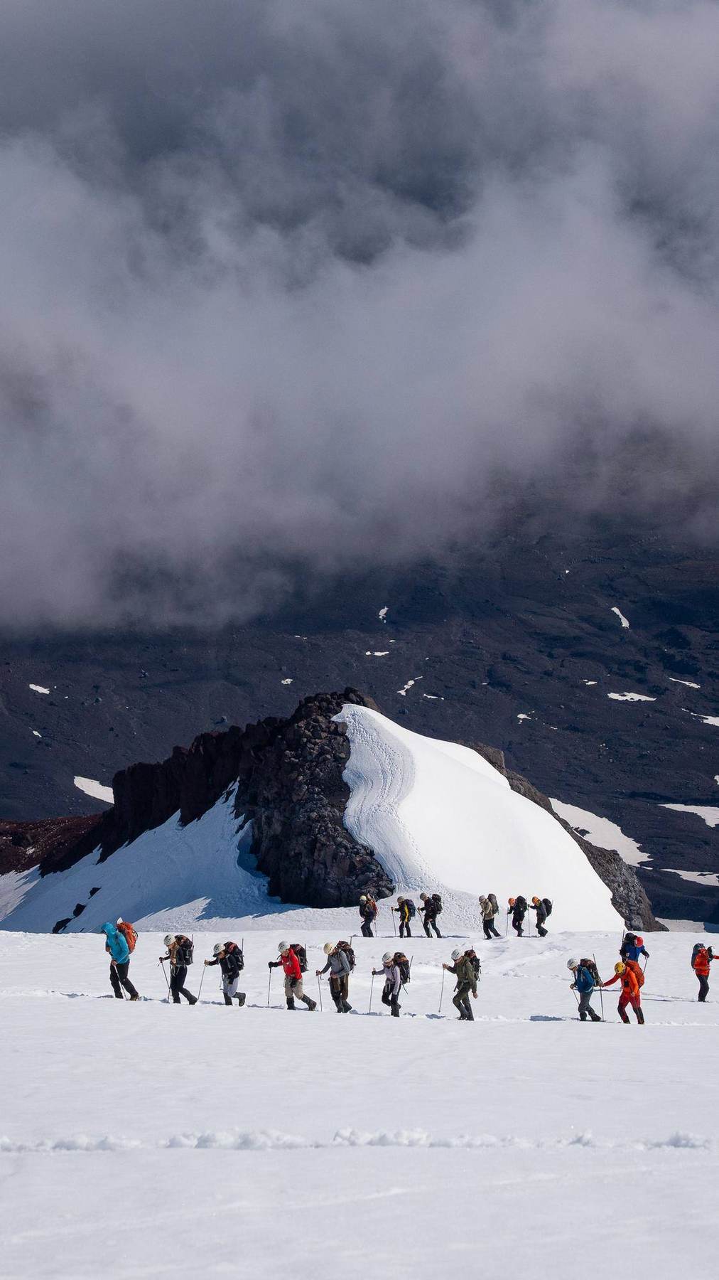 Die Gruppe durchquert ein dunkles Aschetal auf dem Weg zum schneebedeckten Vulkan