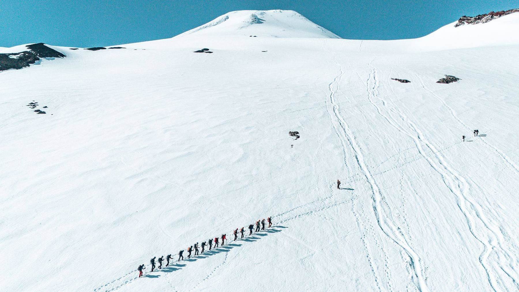 Die Gruppe im Gänsemarsch auf einem weiten Schneefeld, der Gipfel klein in der Ferne