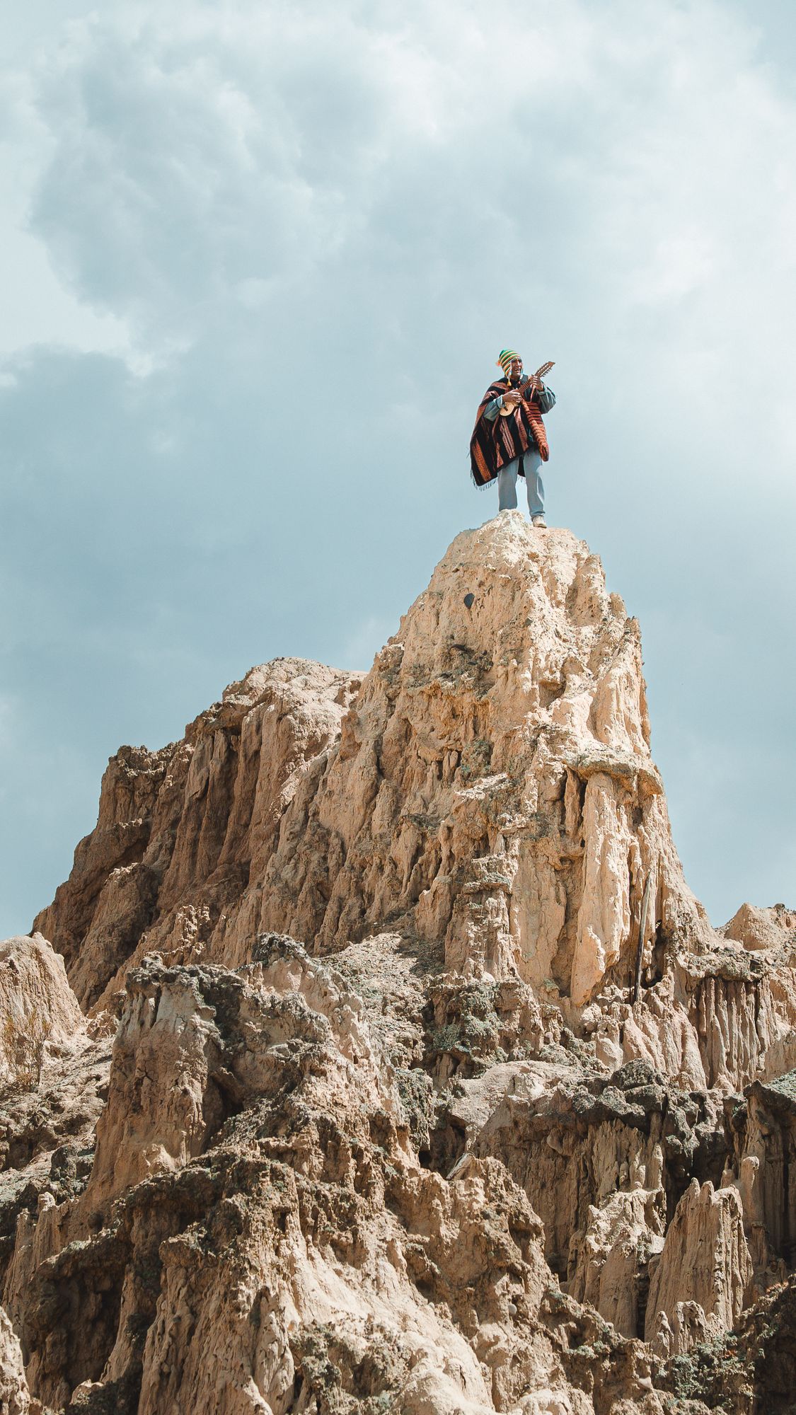 Musiker mit Poncho spielt Charango auf einer Felsspitze im Valle de la Luna, Bolivien