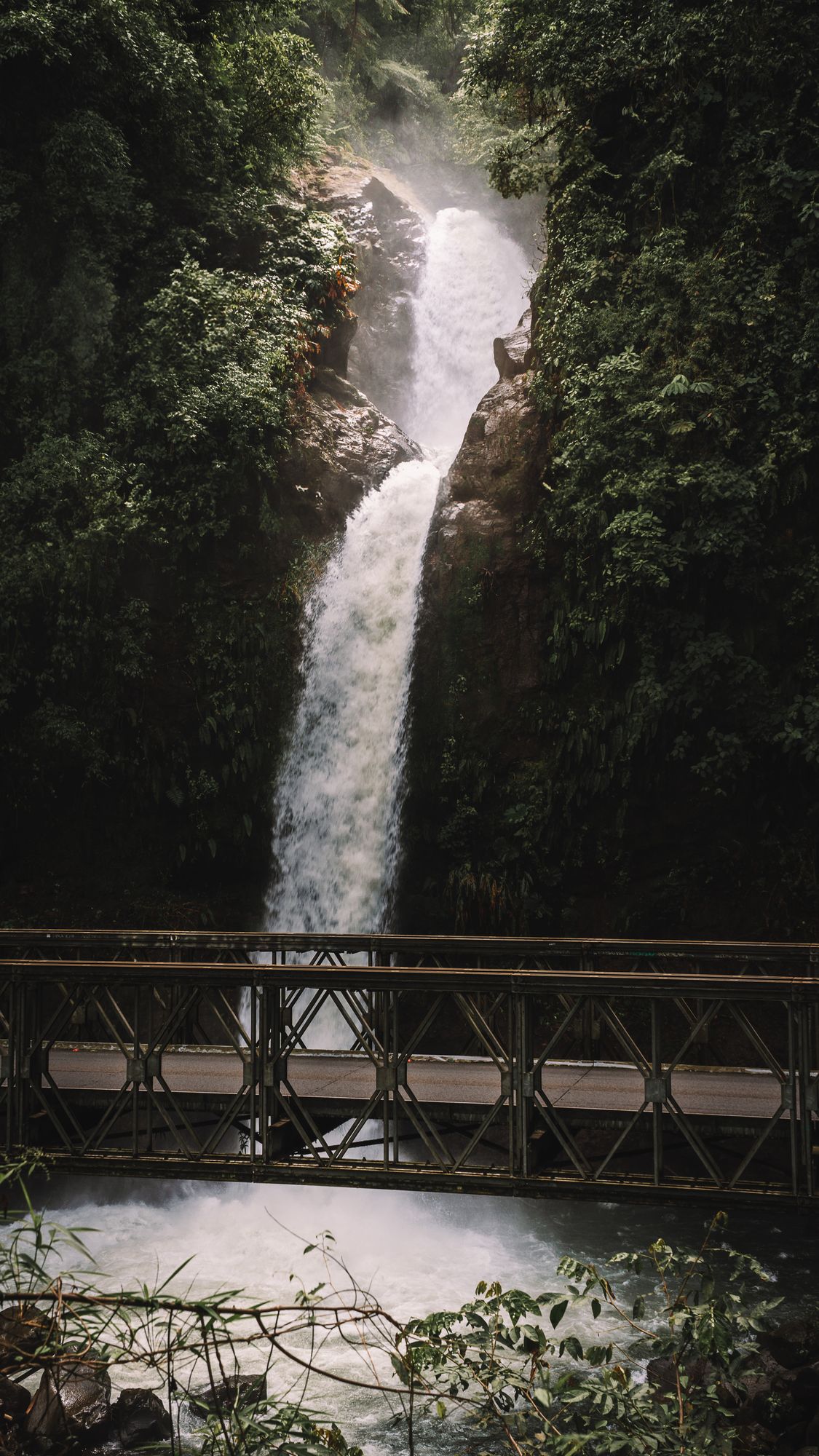 Wasserfall stürzt neben einer Stahlbrücke durch den Dschungel