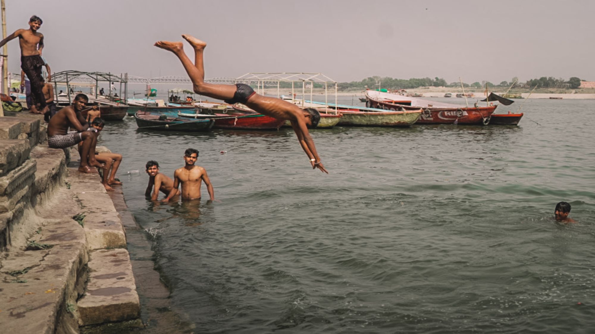 Junge springt kopfüber in den Ganges zwischen den Booten von Varanasi